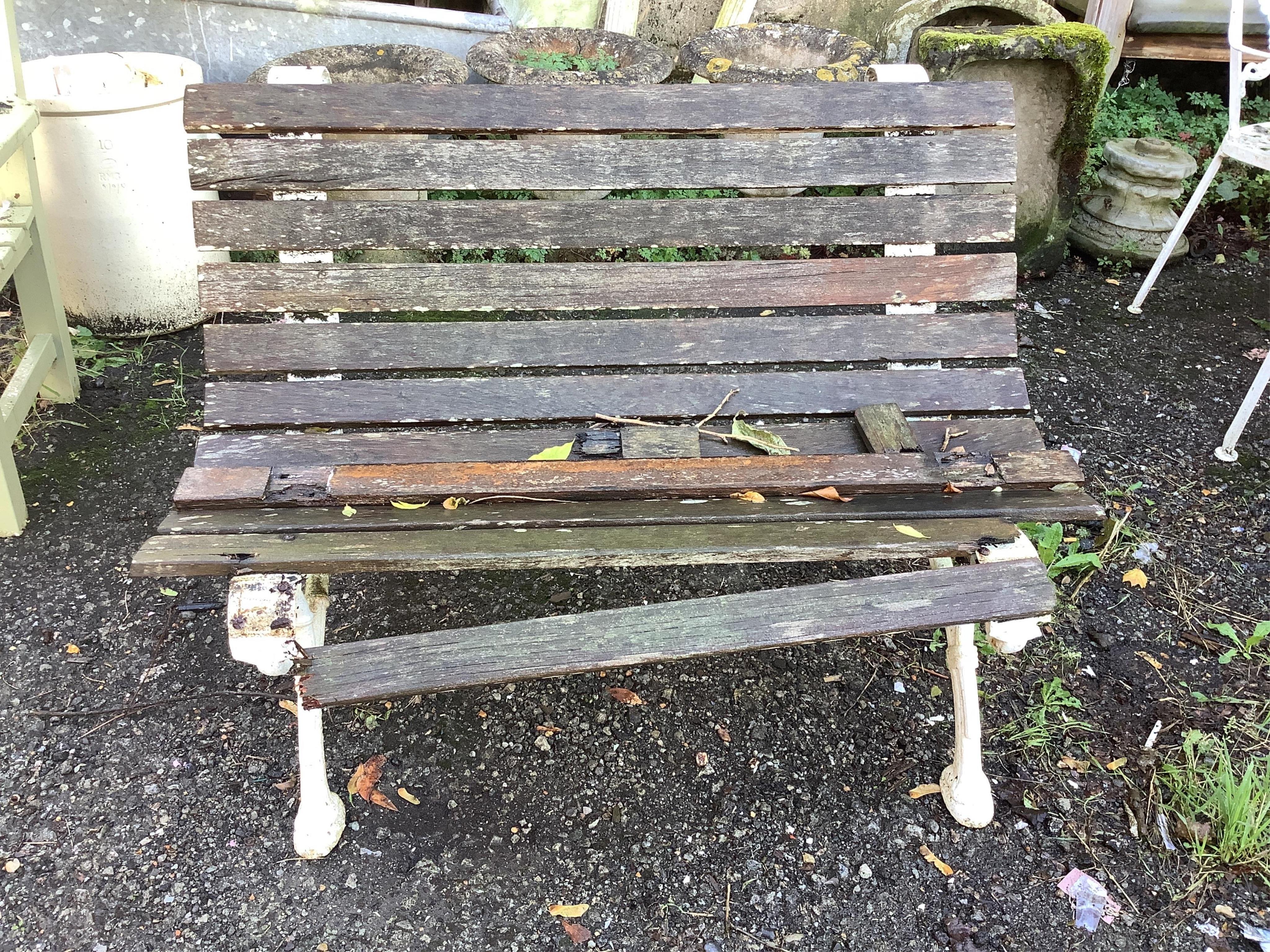 A Victorian slatted teak garden bench, raised on white painted cast iron ends, width 109cm, depth 70cm, height 74cm. Condition - poor